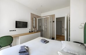 Habitació d'hotel moderna amb un llit, televisió penjada a la paret, zona de dutxa i una cadira verda.