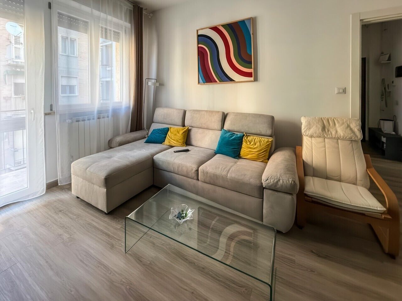 Un salon moderne avec un canapé d’angle, une table basse en verre et un fauteuil en bois.