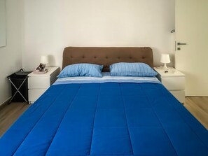 Ein Bett mit blauer Bettdecke, zwei Kissen, einem Holzkopfende und zwei Nachttischen mit Lampen.