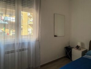 Ein Schlafzimmer mit einem Bett, einem Nachttisch, einem Spiegel und einem Fenster mit Vorhängen.