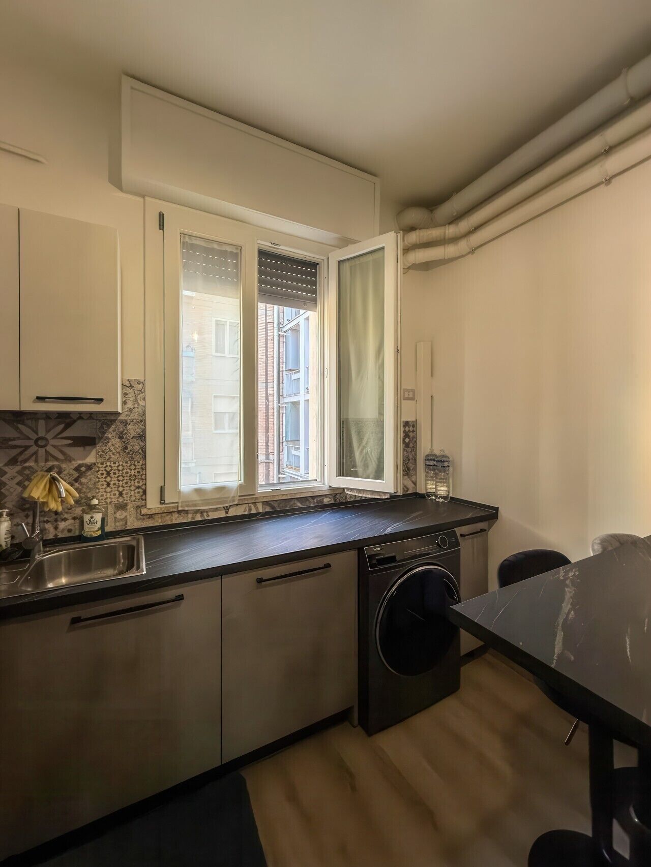 A compact kitchen with a washing machine, a sink, and a window with curtains.