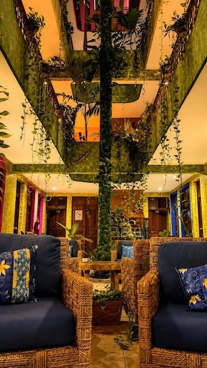 A lobby with wicker furniture, a central column with hanging plants, and a warm color scheme. - Hotel Kaa Zahil (Playa del Carmen)