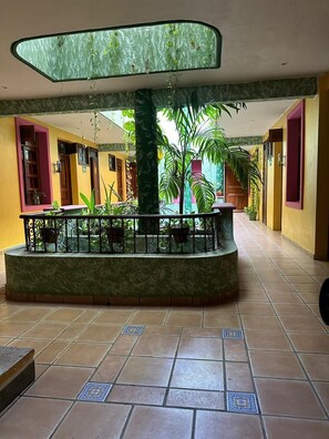 A spacious indoor area with a central column, tiled flooring, and potted plants.