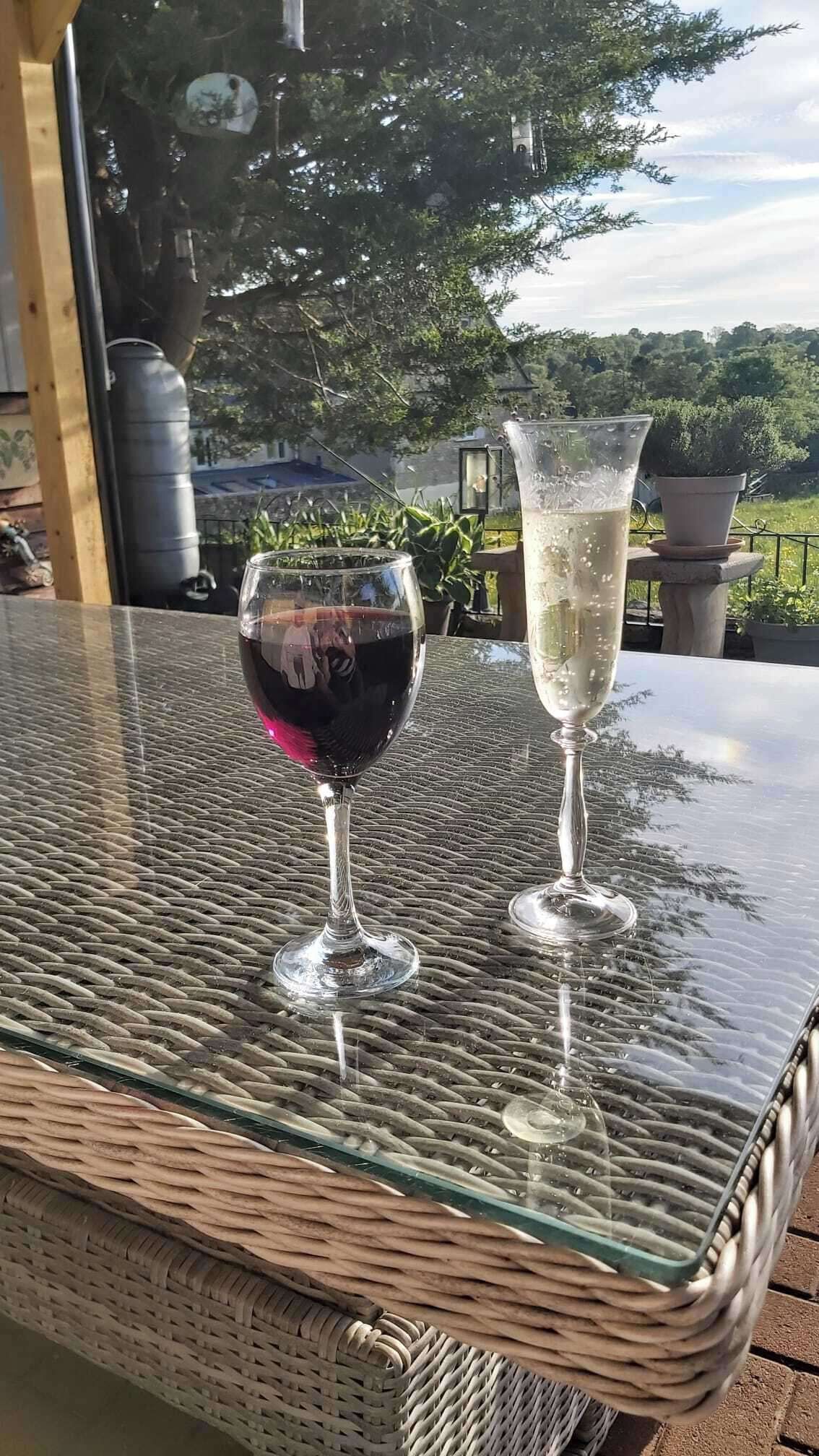 Two glasses of wine on a glass table with a view of trees and a building in the background.