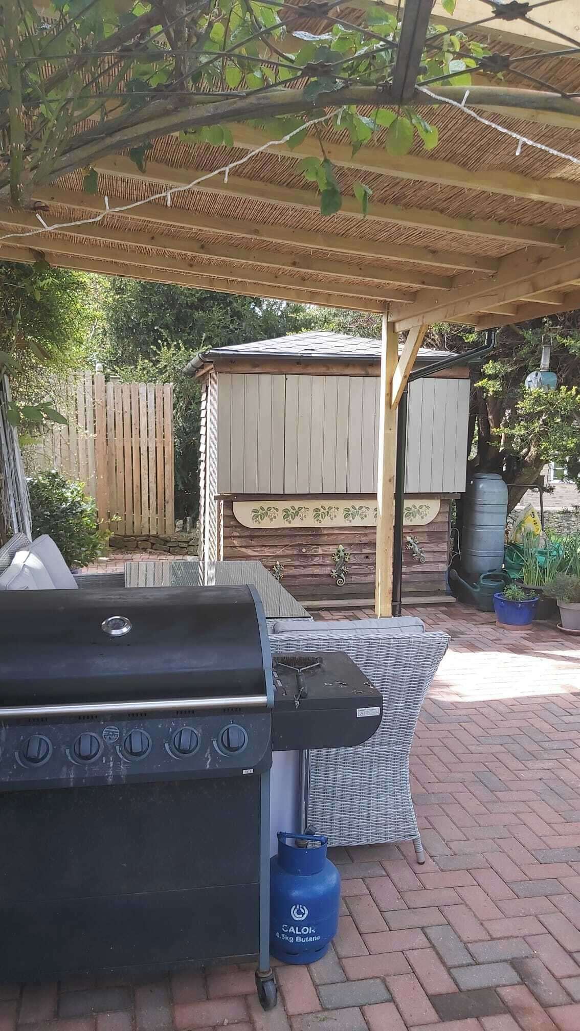 A barbecue grill, a blue propane tank, and a covered seating area with a thatched roof.