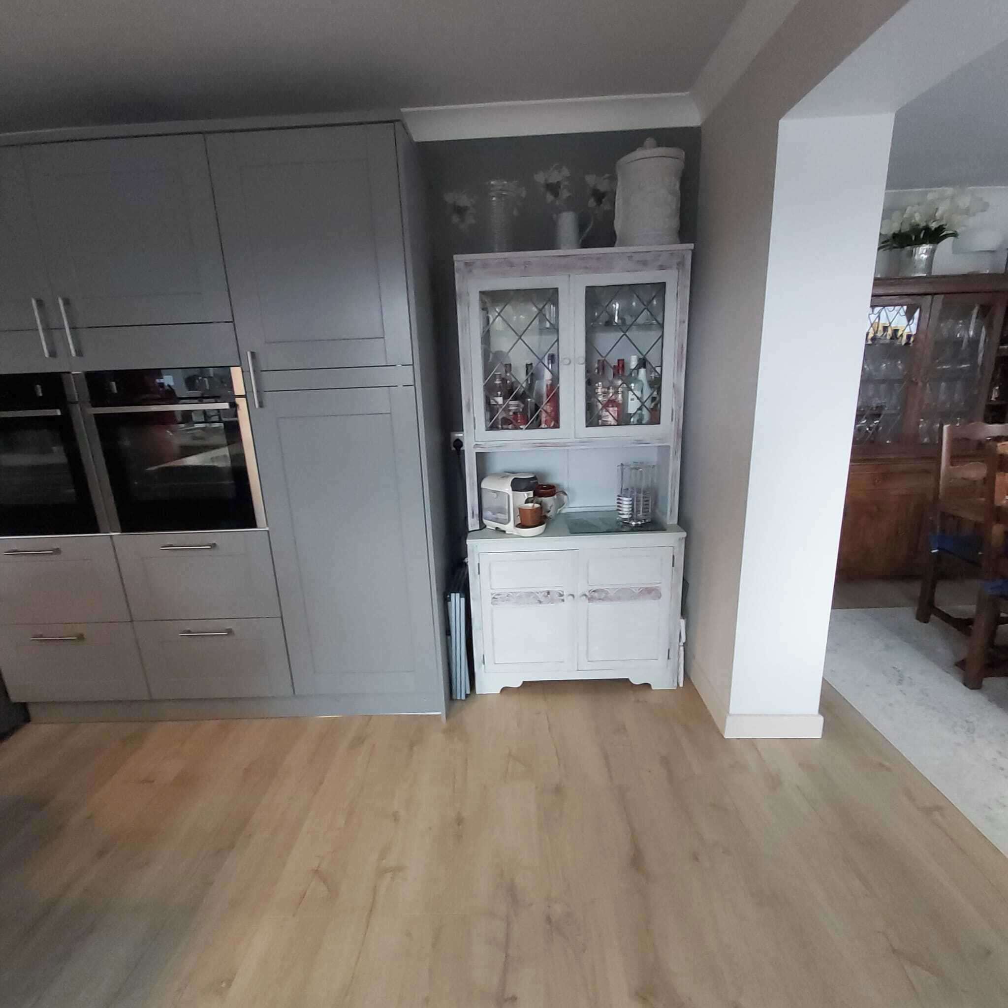 Uma cozinha com armários cinza, um armário branco com portas de vidro e uma mesa de jantar de madeira.