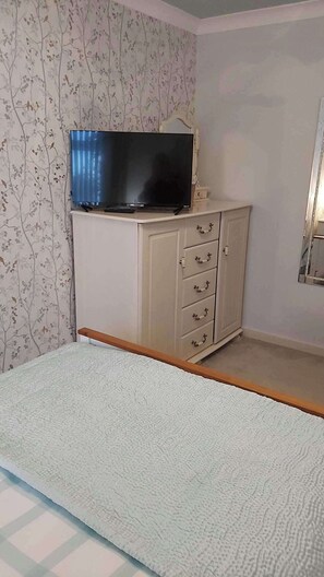 Um quarto com cama, cômoda, televisão e espelho.