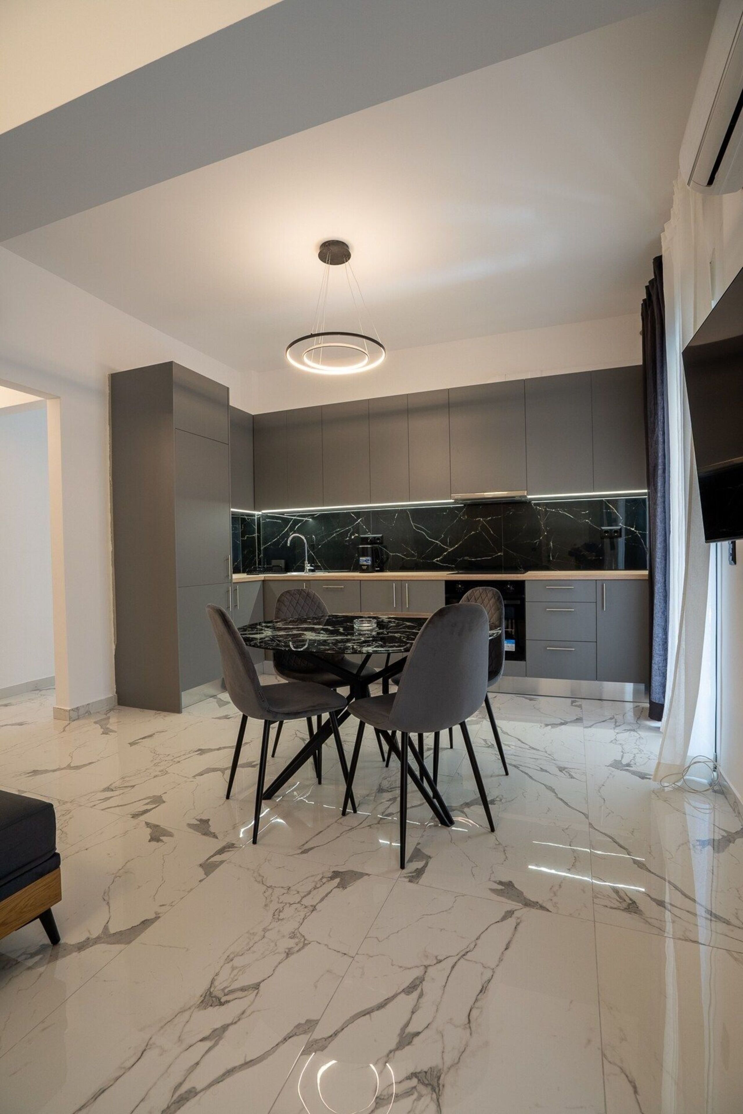 A modern kitchen with dark cabinetry, a marble countertop, and a dining area with a marble table and chairs.