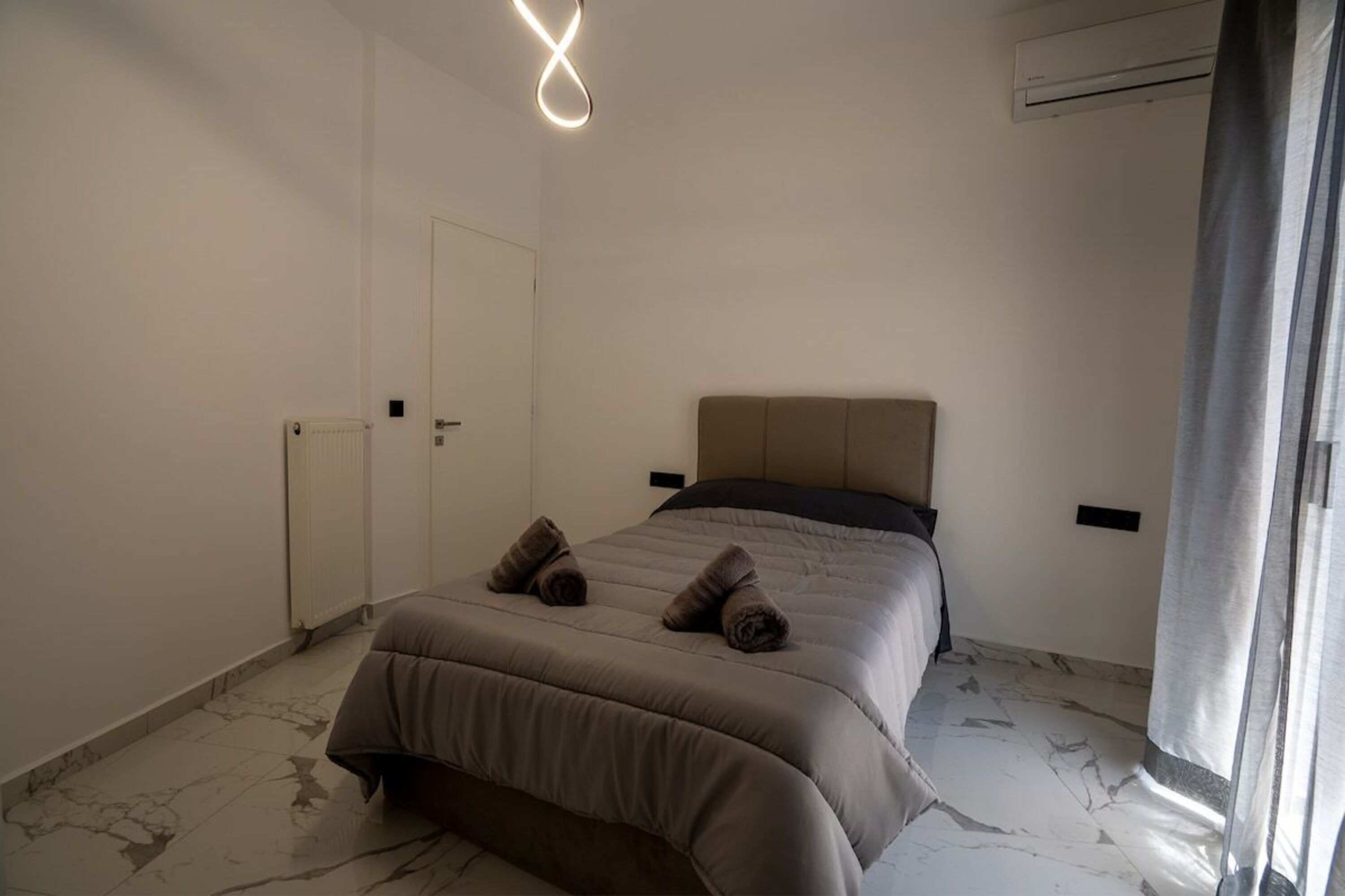 A bedroom with a bed, a radiator, an air conditioning unit, and a door.