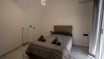 A bedroom with a bed, a radiator, an air conditioning unit, and a door.