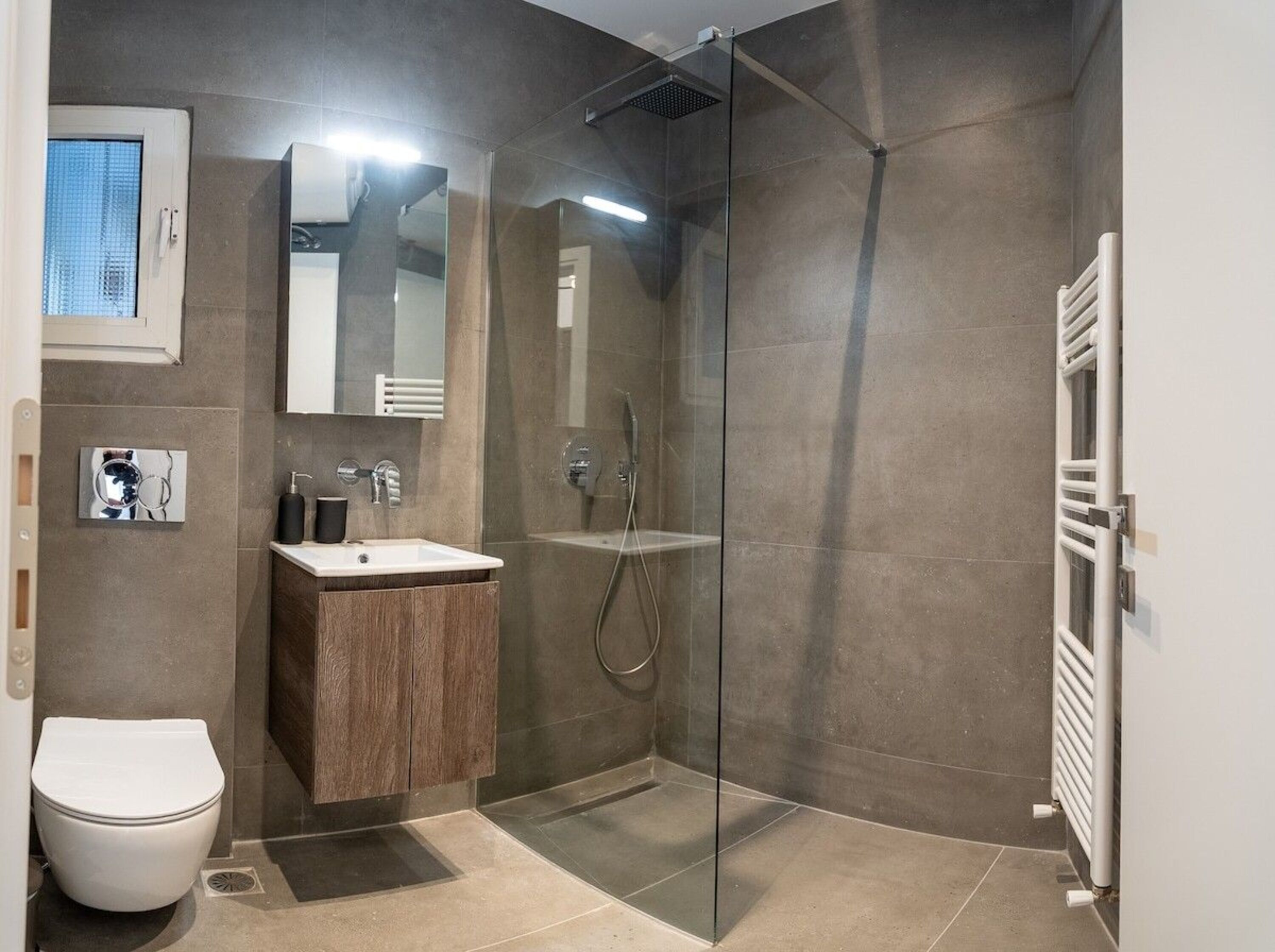A modern bathroom with a glass-enclosed shower, a wooden vanity, a white toilet, and a mirror above the sink.