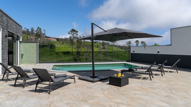 Uma área de piscina com espreguiçadeiras, uma mesa com bebidas e um grande guarda-sol.