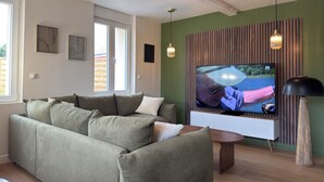 Een woonkamer met een bank, een televisie, een houten accentmuur en een plafondventilator.