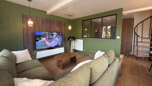 Een woonkamer met televisie, bank, houten vloer en een trap.