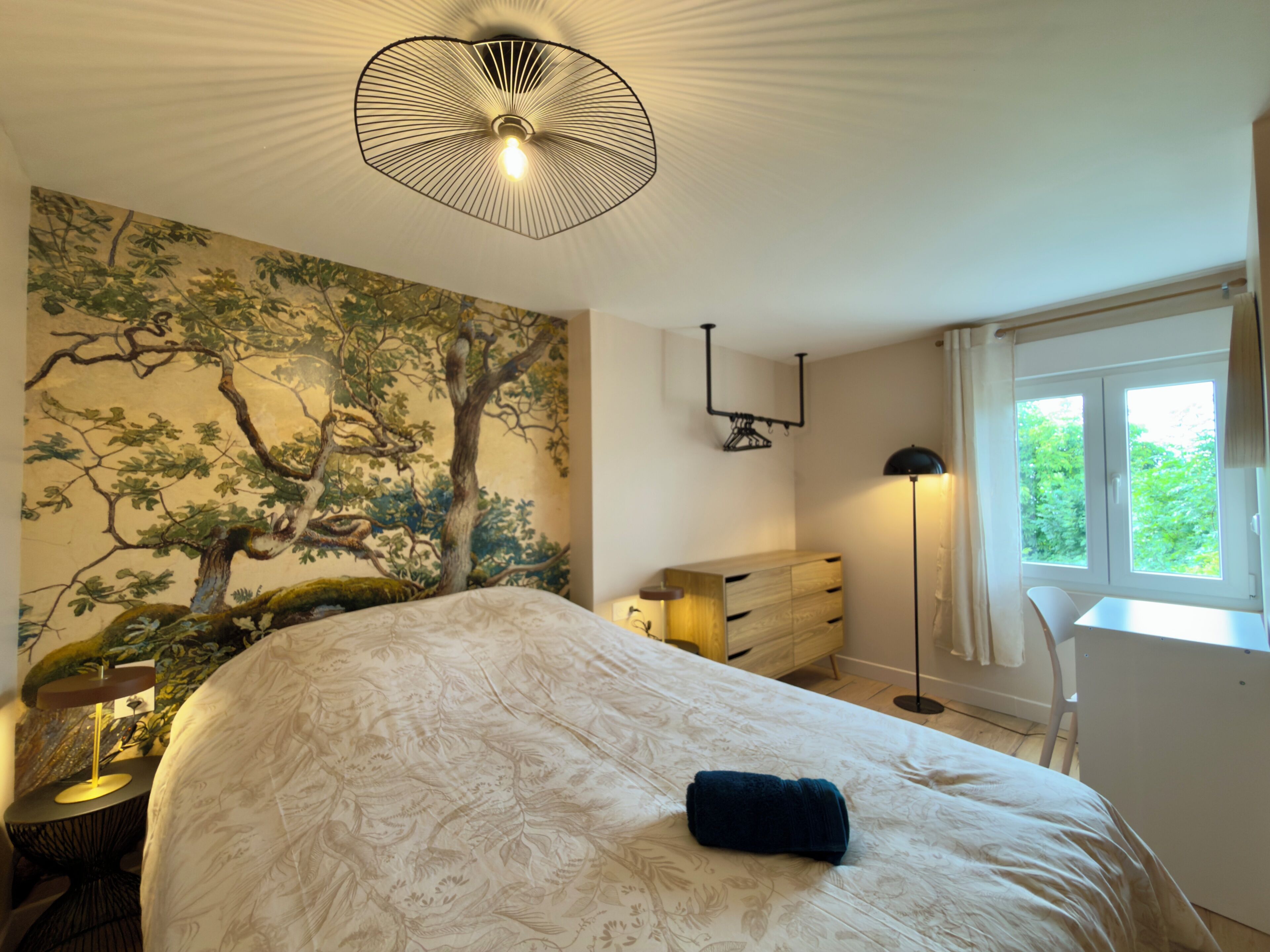 Une chambre avec un grand lit, une peinture murale, un bureau et une fenêtre.