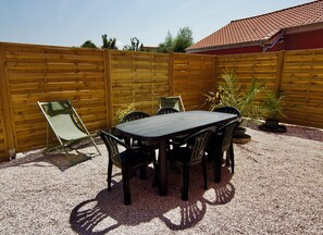 A patio with a table and chairs, surrounded by a wooden fence and gravel ground. - Cozy house, garden, barbecue, 2 parking spaces, 5 minutes from Gravelines (Saint-Folquin)