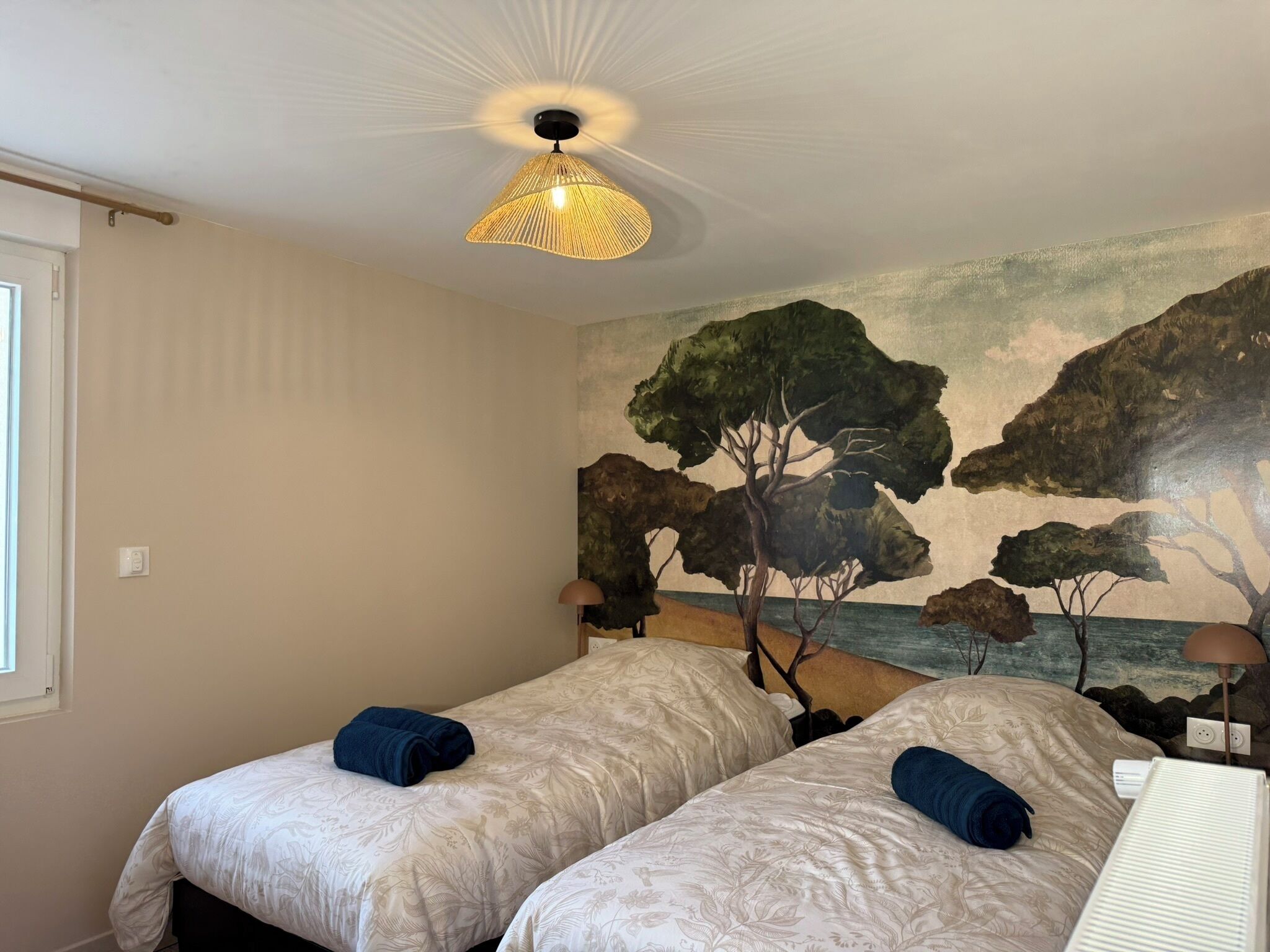 A bedroom with two beds, a ceiling fan, and a mural on the wall.