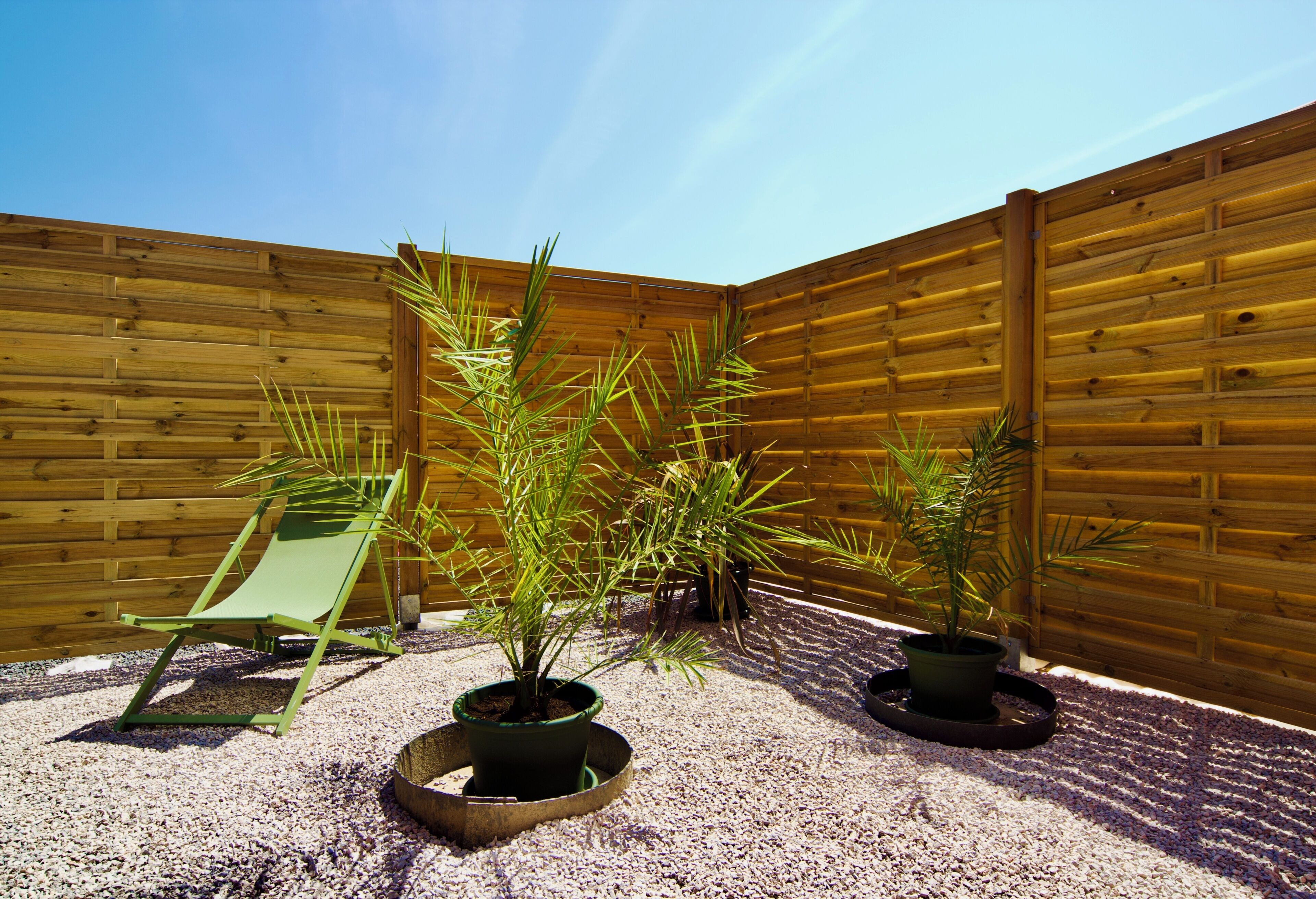 A wooden fence, a green chair, and potted plants in a garden area.