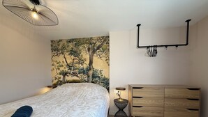 Een slaapkamer met een bed, een houten dressoir, een wandlamp en een wandtapijt.