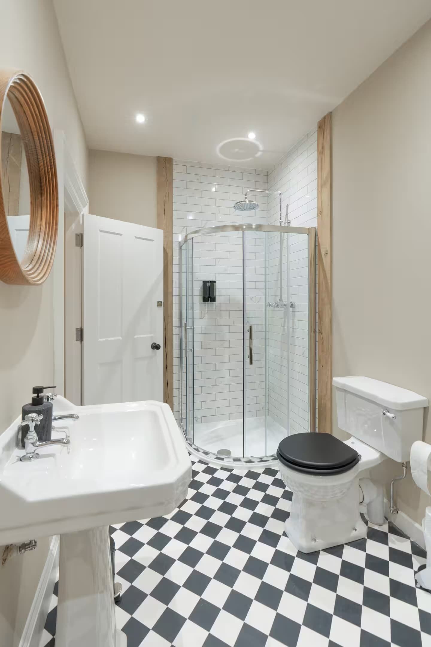 Un bagno con pavimento a scacchi, un lavandino bianco, un WC, box doccia in vetro e uno specchio con cornice in legno.