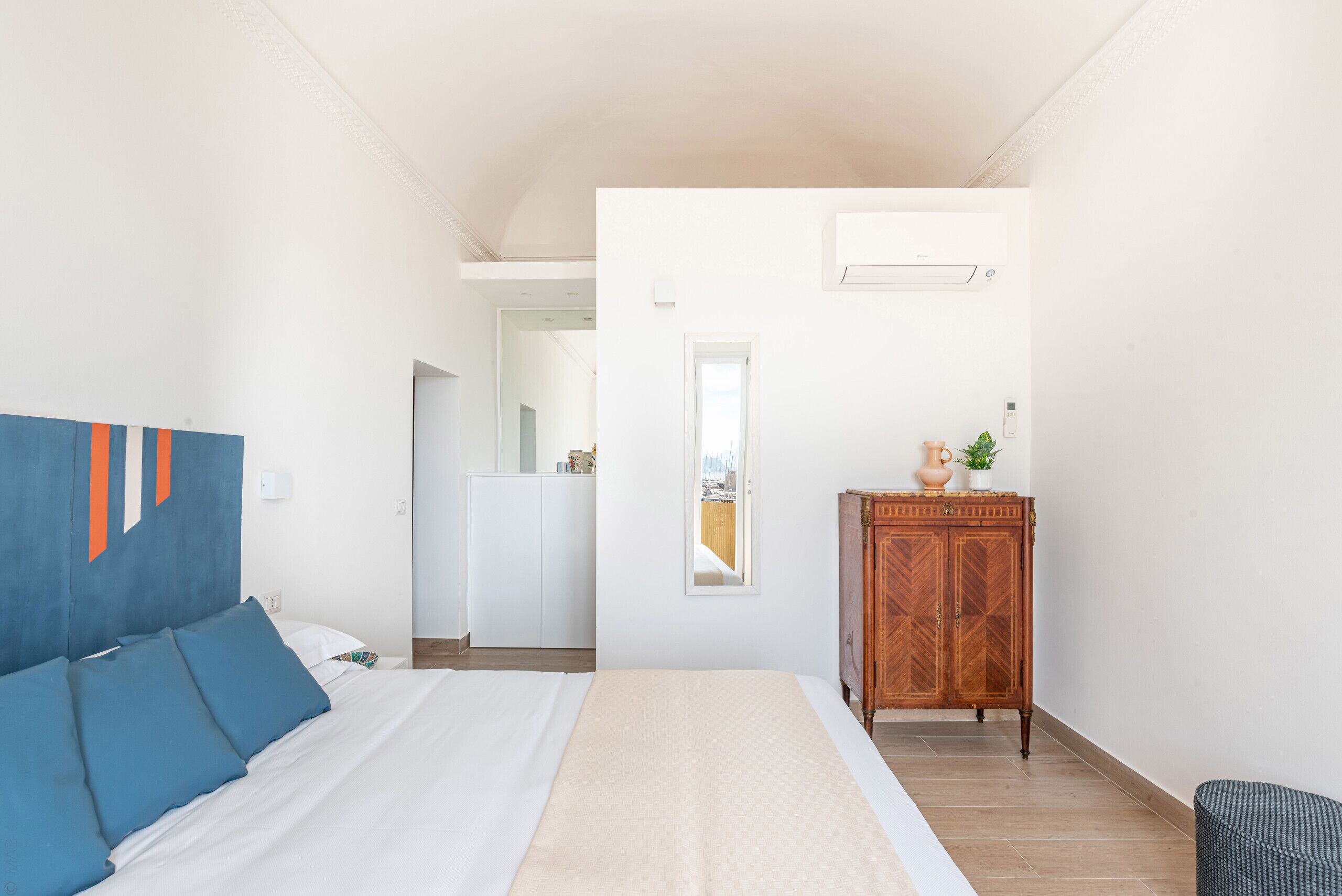 A bedroom with a bed, a wooden cabinet, and a view of a kitchen.