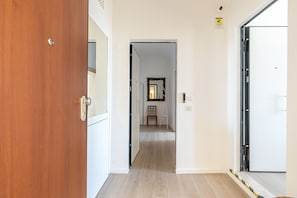 A hallway with a wooden door on the left, a white door on the right, and a mirror on the wall. - Igiea Florio Sea View by Wonderful Italy (Palermo)