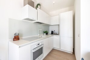 Una cuina moderna amb armaris blancs, una campana extractora d'acer inoxidable, un forn integrat i un taulell amb una planta i utensilis de cuina.