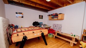 Tunnelmallinen huone, jossa on pöytäjalkapallopeli, puinen penkki ja hylly, jossa on kirjoja ja leluja.