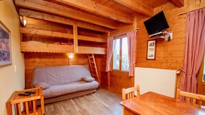 Tunnelmallinen mökin sisustus, jossa on sohva, puinen ruokapöytä ja seinälle asennettu televisio.