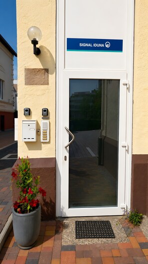 A building entrance with a door, a sign reading 'SIGNAL IDUNA,' and a potted plant with red flowers. - Modern Apartments in the Heart of Hildesheim (Hildesheim)