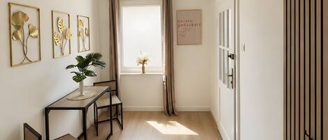 A hallway with a wooden floor, a table with chairs, a potted plant, and a window with curtains.