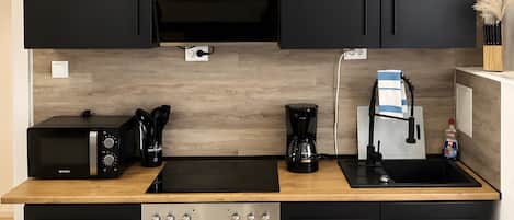 Una cocina moderna con armarios negros, encimera de madera, horno empotrado, cocina y cafetera.