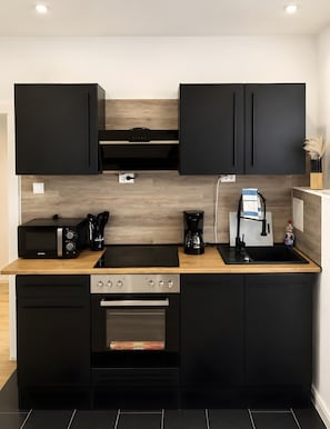A modern kitchen with black cabinetry, a wooden countertop, a built-in oven, and a coffee maker. - Modern Apartments in the Heart of Hildesheim (Hildesheim)