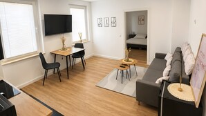 Ein modernes Wohnzimmer mit einer Couch, einem Esstisch und einem an der Wand montierten Fernseher.