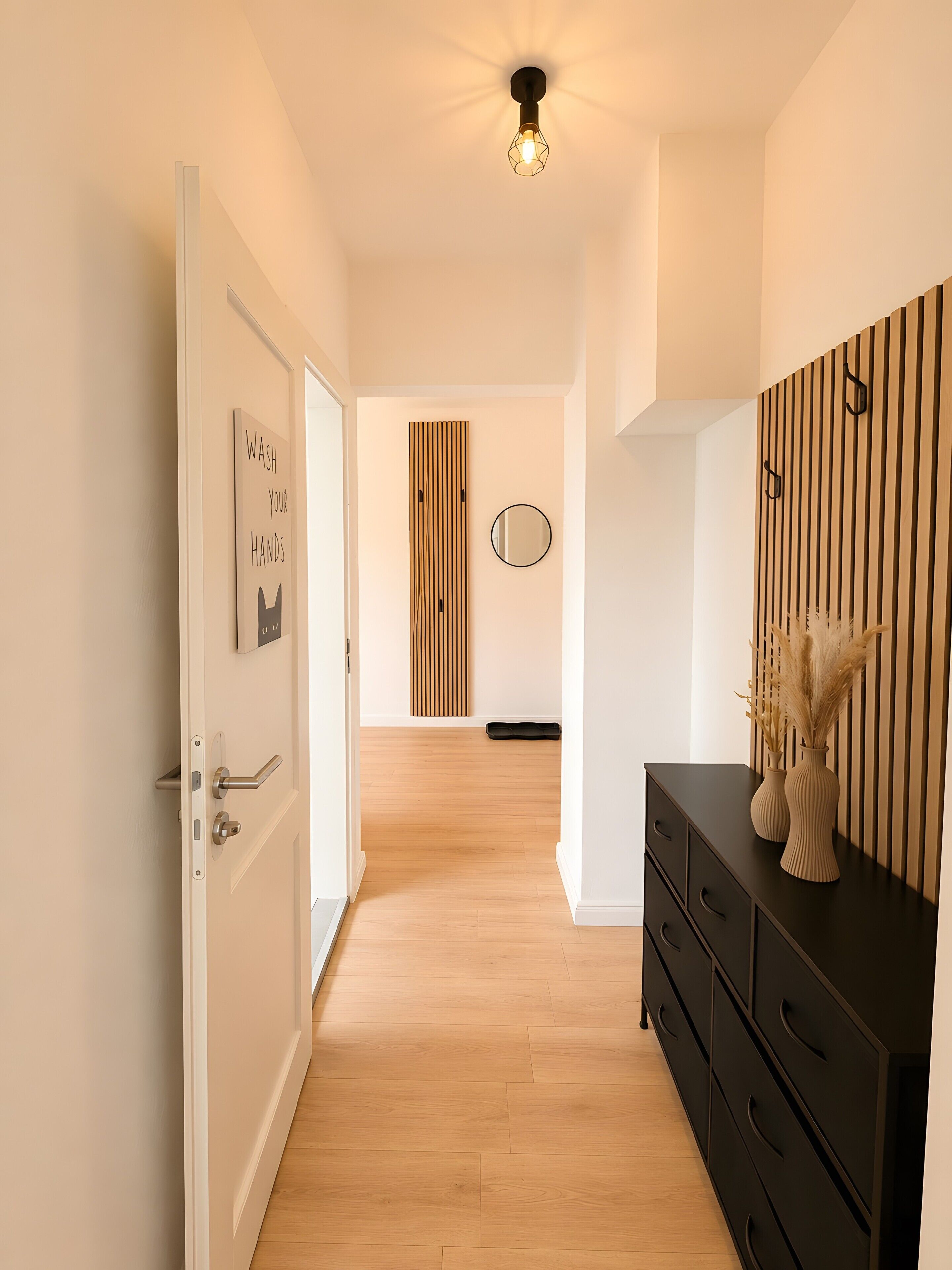 Un pasillo con una puerta, un letrero en la pared, un espejo, un revestimiento de paneles de madera y un aparador negro con jarrones.