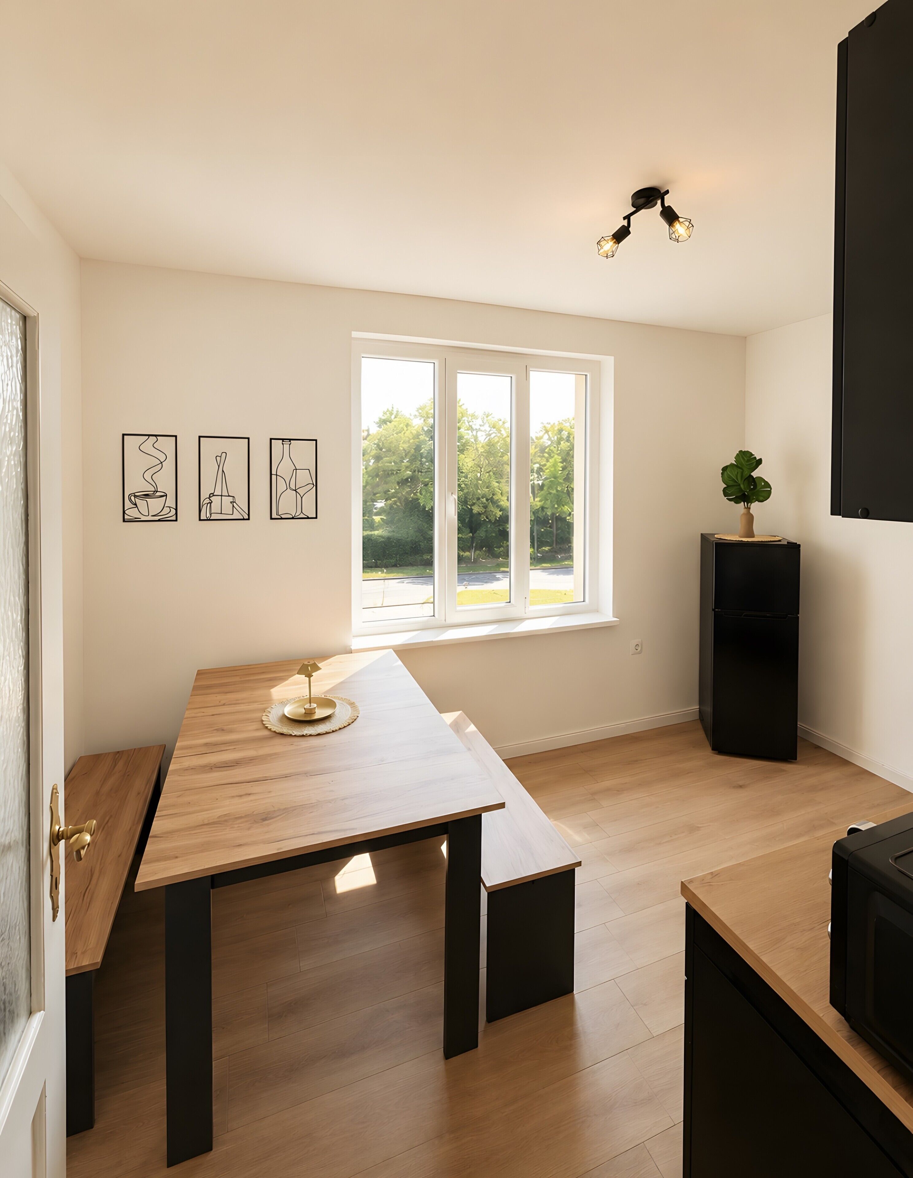A modern kitchen with a wooden table, a window with a view of trees, and a black speaker.