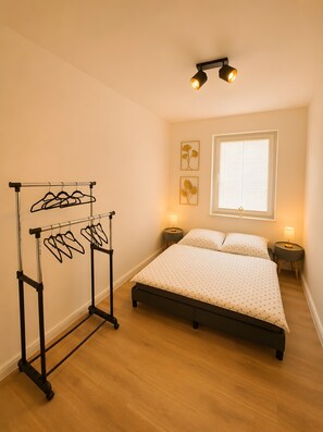 Un dormitorio con cama, perchero, mesitas de noche, ventana con persianas y decoración en la pared.