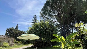 Un jardín con una mesa y sillas de metal, un paraguas a rayas y una planta en maceta.