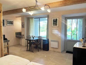 Ein Zimmer mit Esstisch, Stühlen, einem Fernseher, einer Heizung und großen Fenstern mit Vorhängen.