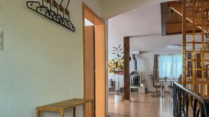 Una panca di legno, un appendiabiti a parete, una pianta in vaso, un camino e un'area pranzo con sedie e tavolo.