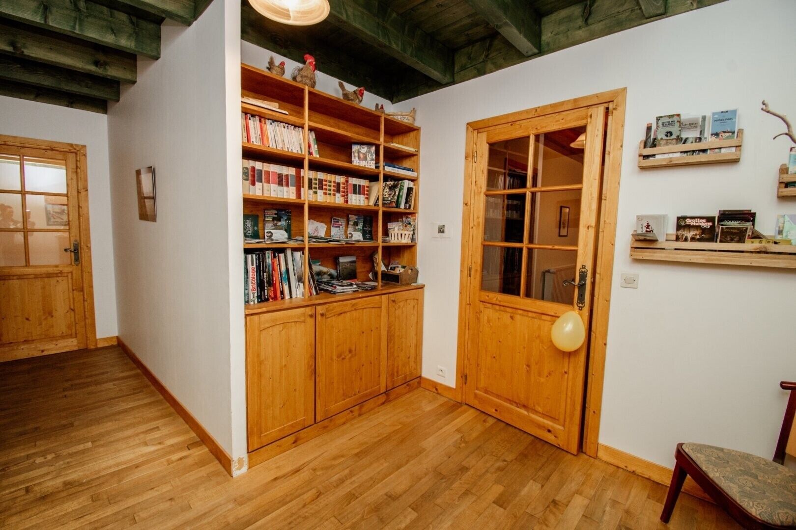 A wooden bookshelf filled with books, a wooden door with a glass panel, and a small wooden shelf with books on the wall.