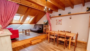 Un acogedor loft con una mesa de comedor de madera, cortinas a cuadros blancos y rojos, un sofá y un televisor.