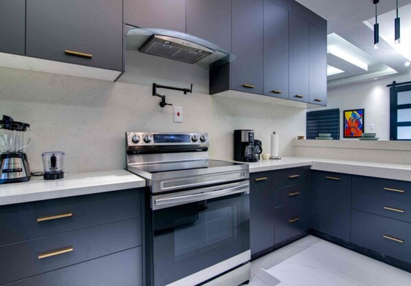 A modern kitchen with dark cabinets, stainless steel appliances, and a coffee maker.