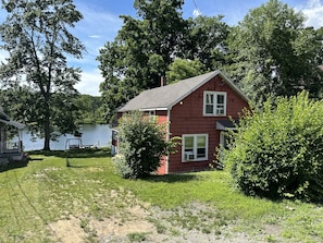 A red house with a porch, a swing, and a lake in the background.