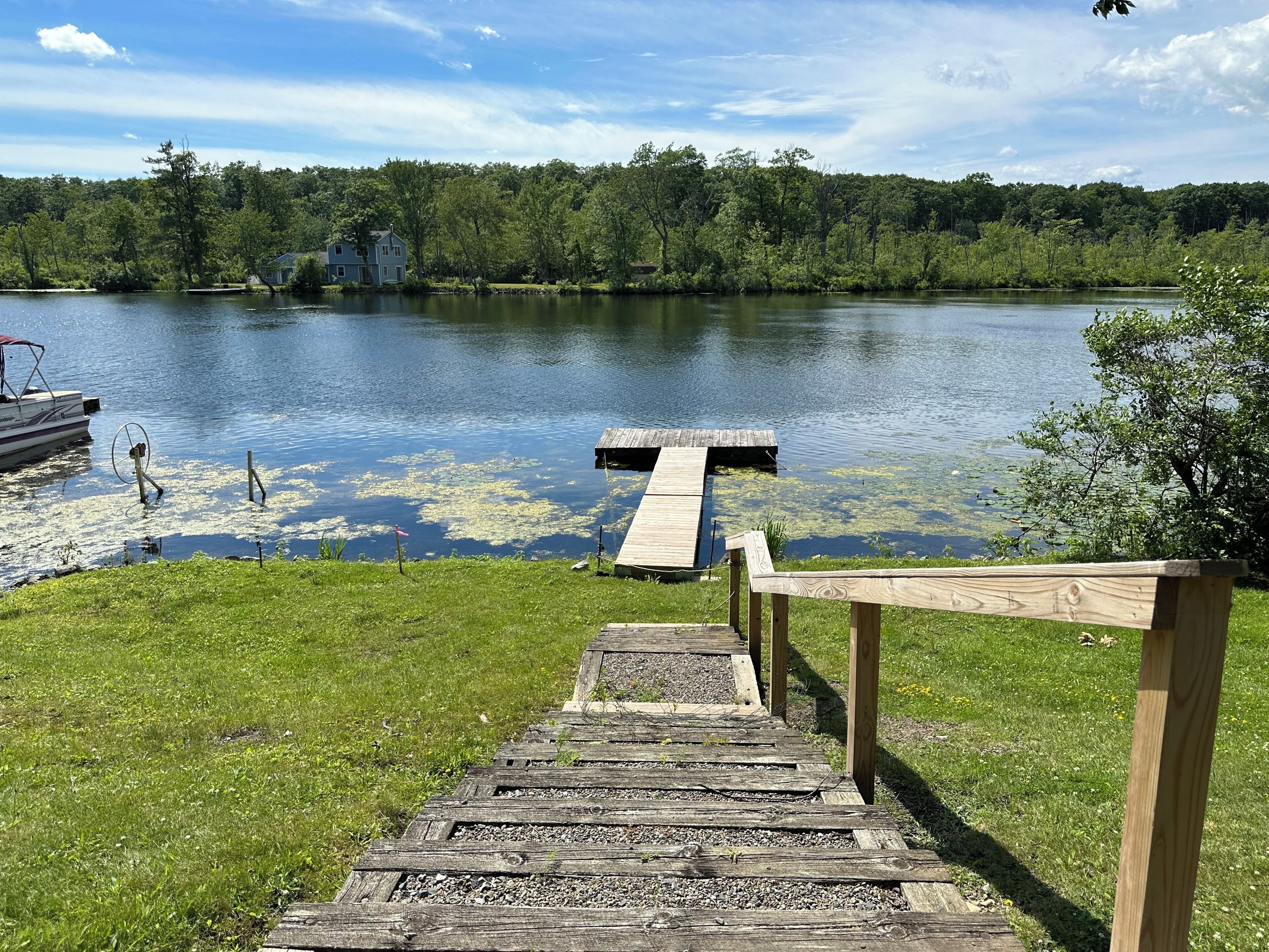 A wooden dock leading to a lake with a house in the background.