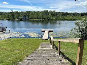 A wooden dock leading to a lake with a house in the background.