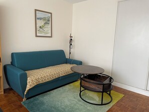 A room with a teal sofa, a patterned throw, a small round table, and a framed picture on the wall. - Spacious, bright, and quiet studio apartment between Paris and La Défense (Asnières-sur-Seine)