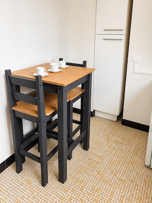 A small kitchen with a wooden table and chairs, a white refrigerator, and a tiled floor. - Spacious, bright, and quiet studio apartment 15 mn from Paris 10 from La Défense (Asnières-sur-Seine)