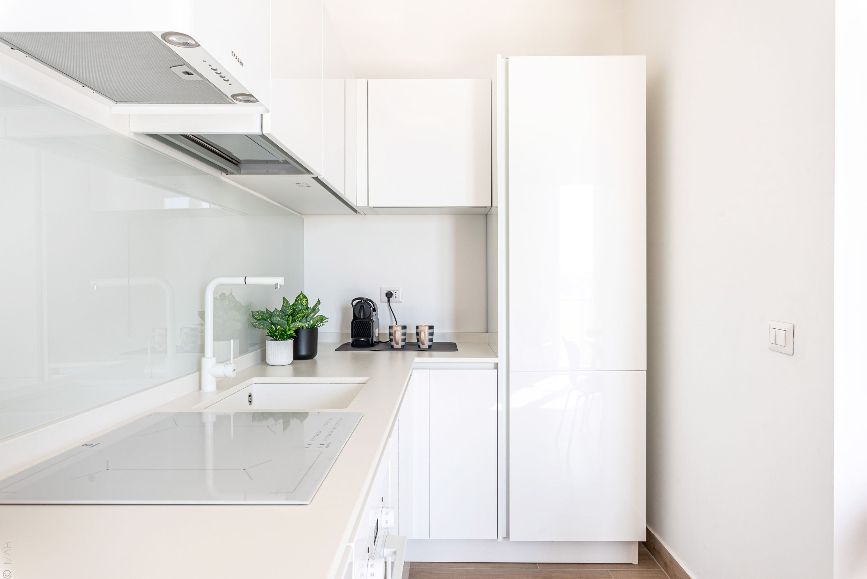 A modern kitchen with white cabinetry, a built-in stove, and a coffee maker on the countertop.