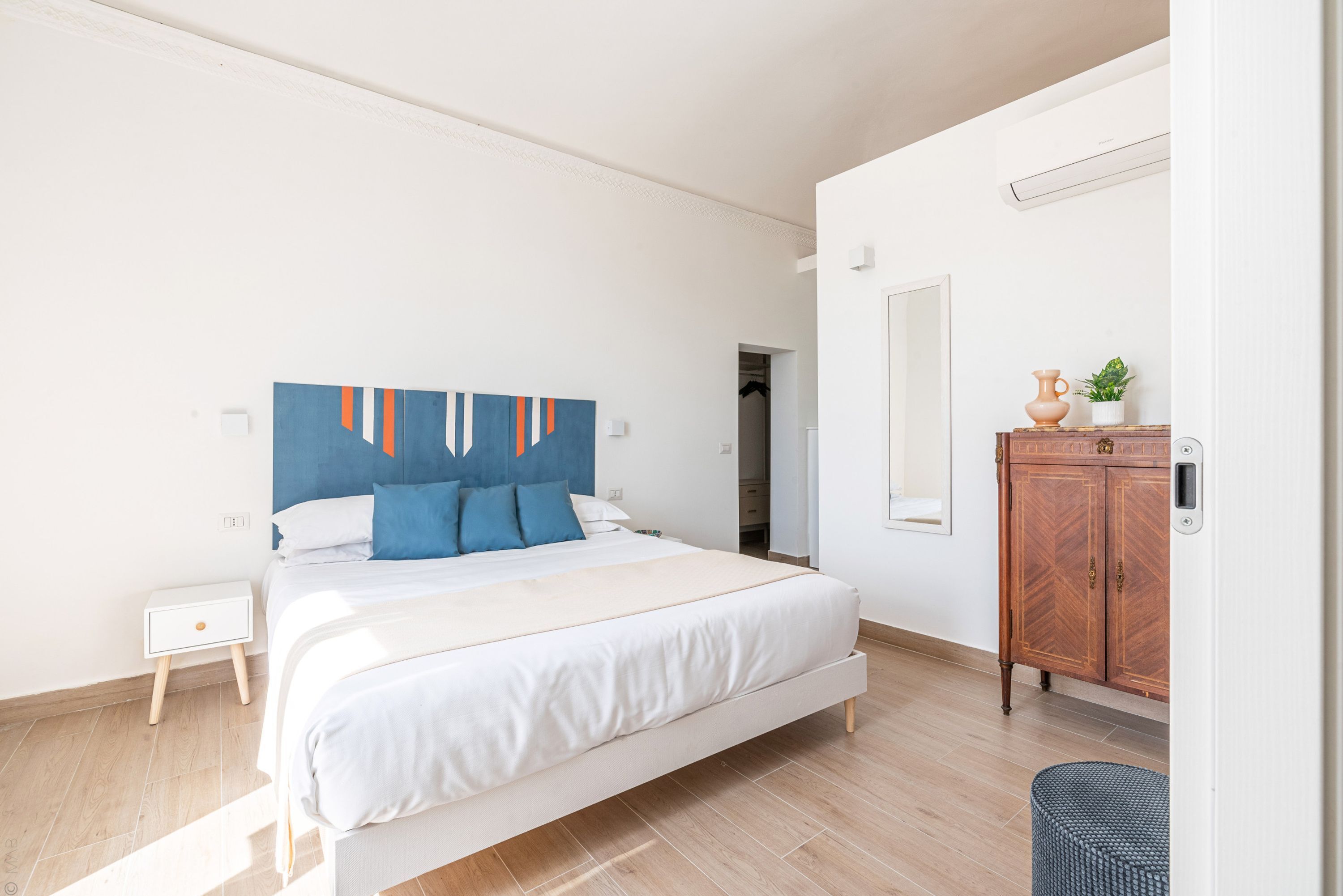 A bedroom with a bed, a nightstand, a wooden cabinet, and a mirror.